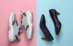 The image shows two pairs of shoes laid side by side on contrasting backgrounds. On the left side, a pair of athletic sneakers in light gray and blue tones are placed on a pink background. On the right side, a pair of navy blue high-heeled shoes are displayed on a light blue background. The juxtaposition of casual sneakers and formal heels creates a visual comparison between comfort and style, highlighting the choice between two different types of footwear.