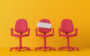 The image shows three red office chairs against a bright yellow background. The middle chair has a blank sign hanging from the backrest, as if it were reserved or indicating availability. The vibrant colors and minimalistic design make it a playful and eye-catching visual, possibly representing job vacancies or opportunities.